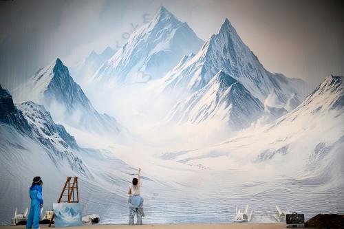 Bühnensituation. Ein bildfüllender Vorhang mit dem Gemälde eines schneebedeckten Bergpanoramas. Eine Person mit einem halb geöffneten grauen Ganzkörperanzug steht mit dem Gesicht zum Vorhang und streckt eine Hand in die Höhe. Eine weitere Person steht etwas entfernt und schaut sie an. An einer Holzleiter lehnt eine kleinere Version des Gemäldes.