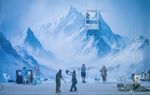 Das Ensemble steht verteilt auf der Bühne. Samuel Weiss hat keinen Kopf mehr. Sachiko Hara hält seinen Kopf in den Händen. Sasha Rau steht in einer hängenden Gondel. Im Hintergrund eine schneebedeckte Berglandschaft.
