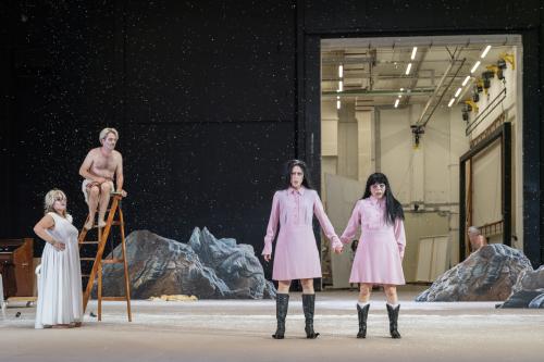 Sasha Rau und Sachiko Hara stehen Hand in Hand nebeneinander, sie tragen beide das gleiche rosa Kleid. Links von ihnen Bettina Stucky und Samuel Weiss, der auf einer Leiter sitzt und einen blutigen Arm in der Hand hält. Im Hintergrund ein Klavier, Felsen und ein offenes Portal zur Hinterbühne.