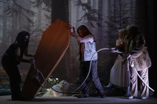Martin Zamorano, Sébastien Jacobs, Sachiko Hara und Bettina Stucky bewegen gemeinsam einen Sargdeckel mithilfe eines Seils. Samuel Weiss befindet sich in einem Loch im Boden. Im Hintergrund das Bühnenbild, das einen düsteren Wald abbildet.