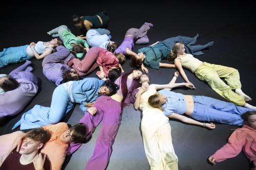 Die Tänzer*innen liegen durcheinander teils ausgestreckt, teils eingerollt auf dem Boden. Alle berühren sich dabei mal mehr, mal weniger.