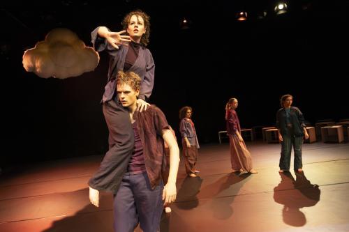 Eine Tänzerin sitzt auf der Schulter eines Tänzers. Sie hält ihre Hand vor sich. Im Hintergrund ist eine Wolke und weitere Tänzerinnen zu sehen. 