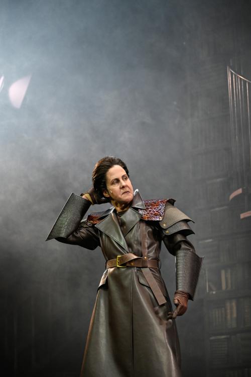 Ute Hannig steht im Nebel und greift sich mit der rechten Hand in die Haare. Sie trägt einen ledernen Mantel und blickt mit heruntergezogenen Mundwinkeln und von oben herab zur Seite.