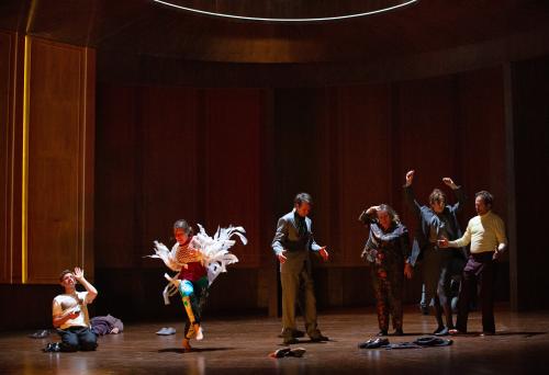 Bühnensituation. Paul Behren, Josefine Israel, Daniel Hoevels, Bettina Stucky, Angelika Richter und Samuel Weiss stehen in einem großen, holzvertäfelten Raum. Sie tragen festliche Kleidung und haben alle die Schuhe ausgezogen. Sie feiern und tanzen. Hinten links liegt Pascal Houdus auf dem Boden. Hinten rechts steht ein Rollstuhl.