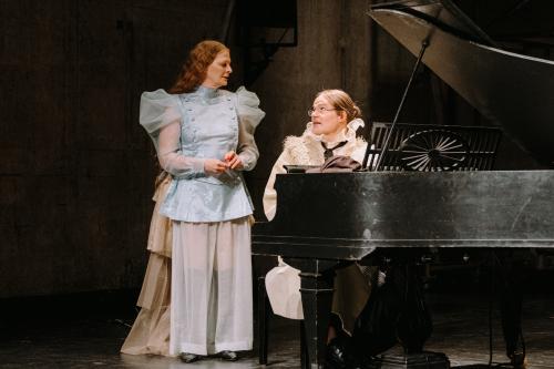 Yorck Dippe sitzt an einem schwarzen Flügel, schaut Christiane von Poelnitz an, die links von ihm steht und ihn auch ansieht. Sie trägt ein Satinoberteil mit Puffärmeln aus Chiffon und zwei Knopfleisten rechts und links. Ihre Hose hat weite, beinahe durchsichtige Chiffonbeine, darunter kann man schwarze Stiefel erkennen. Yorck Dippe trägt einen beigen Mantel mit Fellkragen, darunter einen abstehenden Chiffonkragen. Seine Haare sind zu einem Dutt gebunden, um seinen Hals trägt er eine schwarze Schleife.