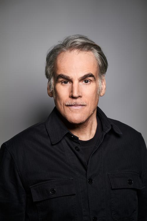 Es ist ein Porträtbild von Sebastian Blomberg vor einem grauen Hintergrund. Er trägt ein schwarzes Oberteil.