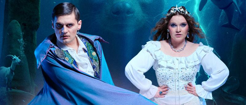 Ein Mann in einem blauen Umhang und Vampirzähnen und eine Frau in einem altmodischen weißen Kleid schauen in die Kamera. Im Hintergrund eine Unterwasserwelt, ein Delfin und der Kopf eines großen Otters.