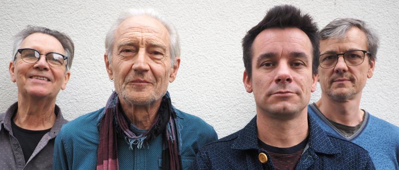 Ruedi Häusermann, Marco Käppeli, Claude Meier, Herwig Ursin stehen eng nebeneinander vor einer weißen Wand und schauen in die Kamera.