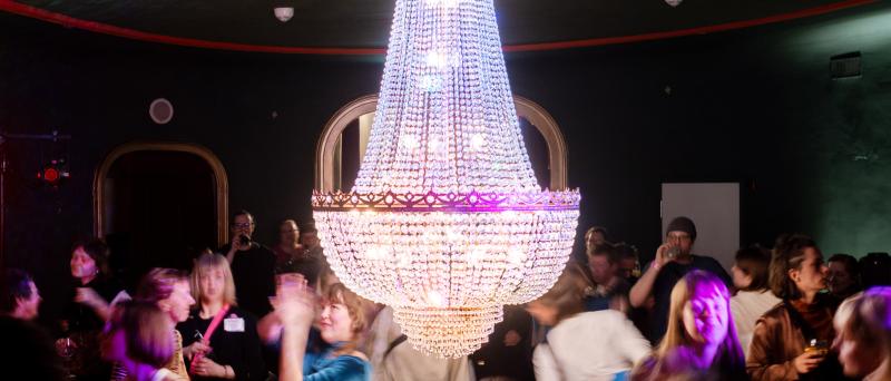 Partyszene. Viele Menschen tanzen unter einem leuchtenden, funkelnden Kronleuchter.