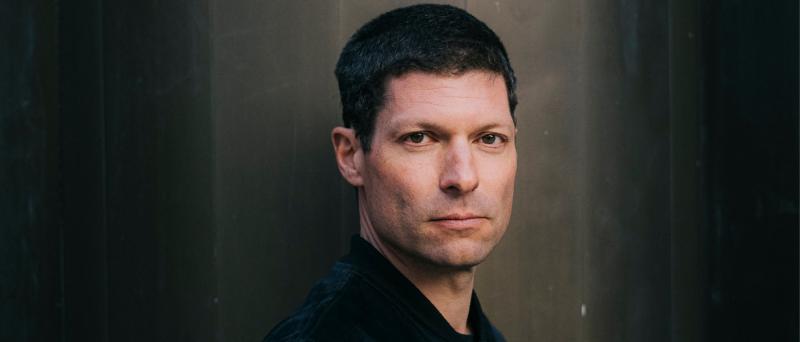 Ronen Steinke steht vor einem neutralen Hintergrund. Er hat kurze dunkle Haare und schaut die Kamera.