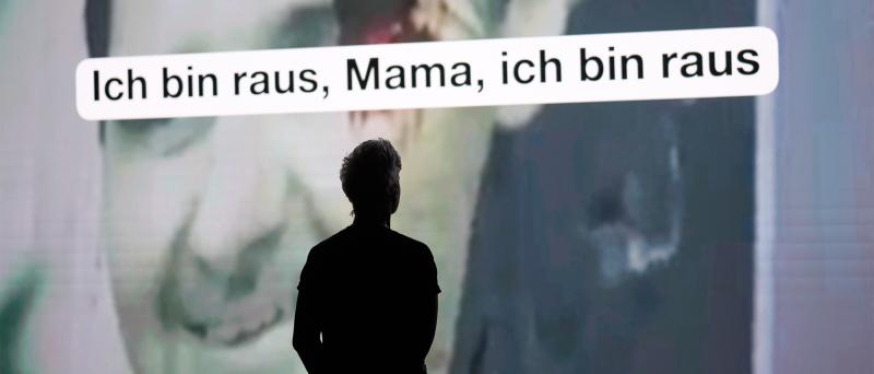 Person als Silhouette vor einer großen Videoprojektion; darüber steht in einem weißen Textfeld: „Ich bin raus, Mama, ich bin raus“.