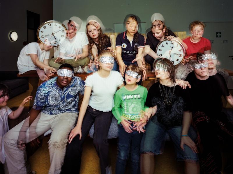 Eine Gruppe von Jugendlichen, einige halten Uhren in der Hand, andere haben einen Streifen Alufolie über den Augen.