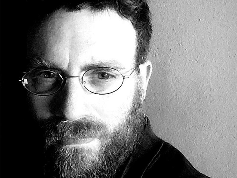 Giorgio Paolo Mastropaolo steht vor einem neutralen Hintergrund. Er trägt eine filigrane Brille, einen Bart und kurze dunkle Haare. Es handelt sich um ein Schwarz-Weiß-Foto.