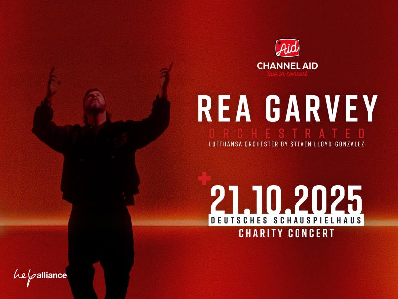 Der Künstler Rea Garvey in schwarzem Pullover vor einem blutroten Hintergrund. Er schaut nach oben und hebt die Arme zum Himmel.