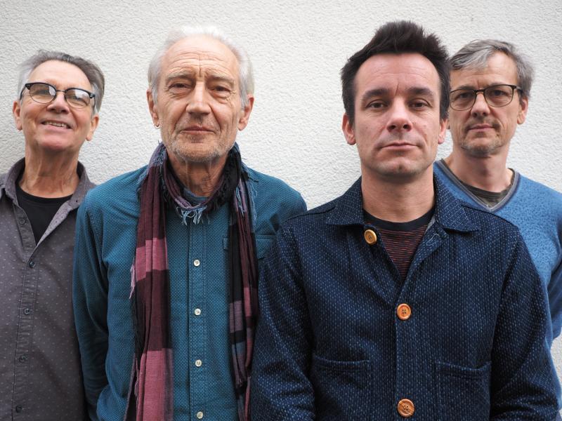 Ruedi Häusermann, Marco Käppeli, Claude Meier, Herwig Ursin stehen eng nebeneinander vor einer weißen Wand und schauen in die Kamera.