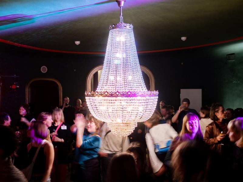 Partyszene. Viele Menschen tanzen unter einem leuchtenden, funkelnden Kronleuchter.