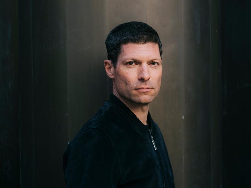 Ronen Steinke steht vor einem neutralen Hintergrund. Er hat kurze dunkle Haare und schaut die Kamera.