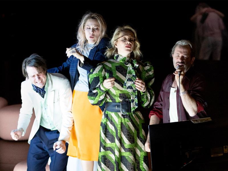 Daniel Hoevels, Josefine Israel, Angelika Richter und Samuel Weiss stehen in einer Reihe und gucken auf einen Fernseher. Samuel Weiss hält ein Mikrofon in der Hand. Alle singen und sind in Bewegung.