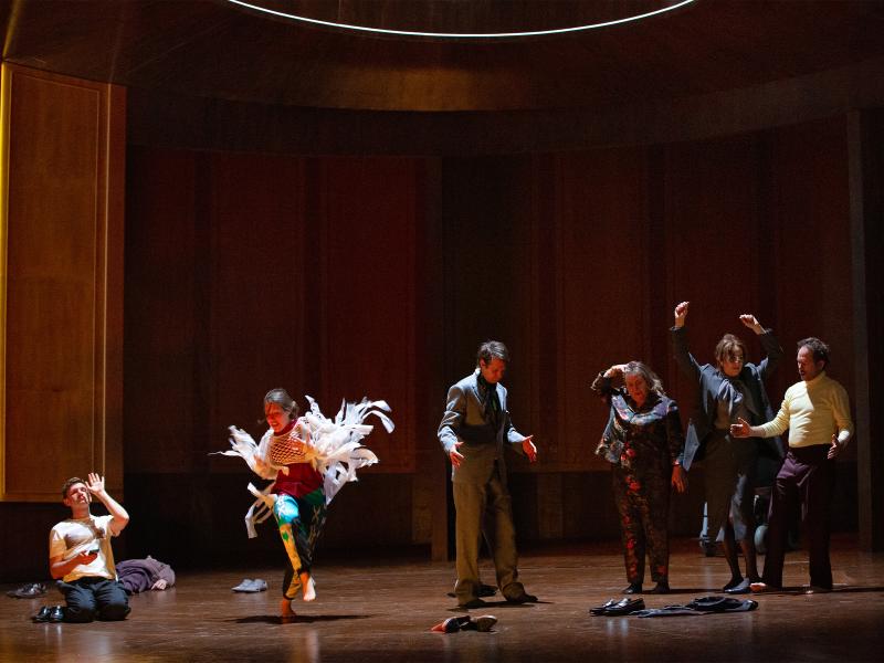 Bühnensituation. Paul Behren, Josefine Israel, Daniel Hoevels, Bettina Stucky, Angelika Richter und Samuel Weiss stehen in einem großen, holzvertäfelten Raum. Sie tragen festliche Kleidung und haben alle die Schuhe ausgezogen. Sie feiern und tanzen. Hinten links liegt Pascal Houdus auf dem Boden. Hinten rechts steht ein Rollstuhl.