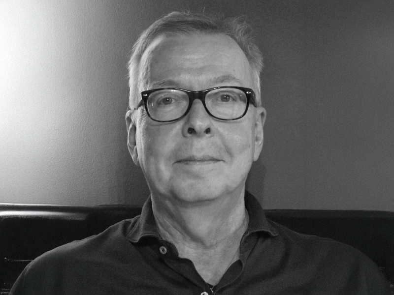 Schwarz-Weiß-Foto. Volker M. Heins trägt ein dunkles Hemd, eine dunkle Brille und kurze Haare. Er sitzt vor einem neutralen Hintergrund.