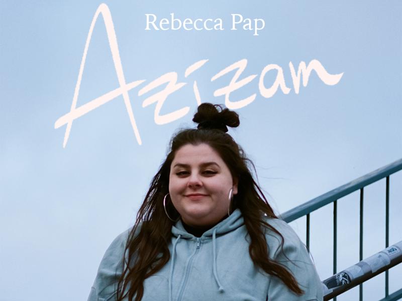Plakat oder Albumcover von Rebecca Paps „Azizam": Eine junge Frau mit hochgestecktem Dutt, langen Creolen und hellblauem Hoodie lächelt vor einem bewölkten Himmel. Titel und Name sind in geschwungener Handschrift über sie gesetzt.