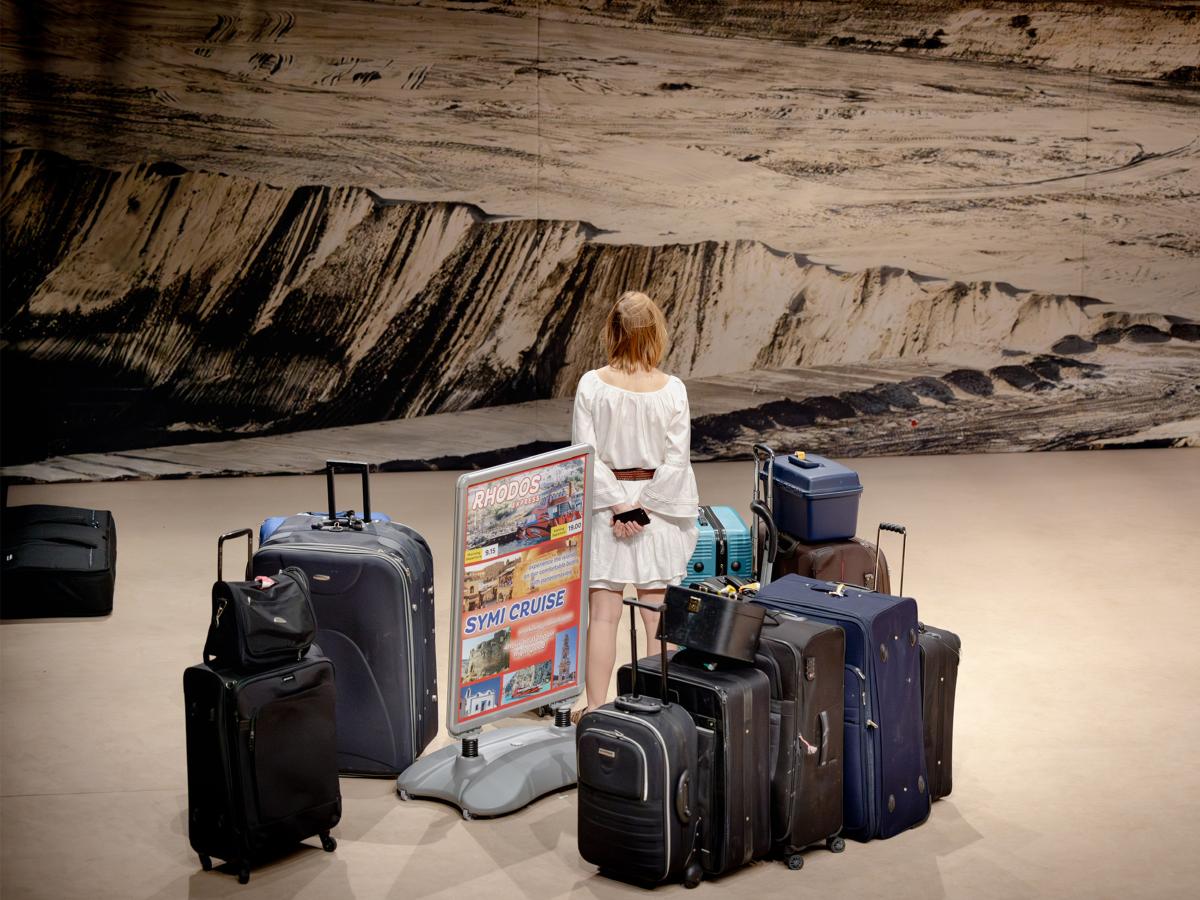 Eine Schauspielerin steht mit dem Rücken zur Kamera, um sie herum ganz viele Koffer.