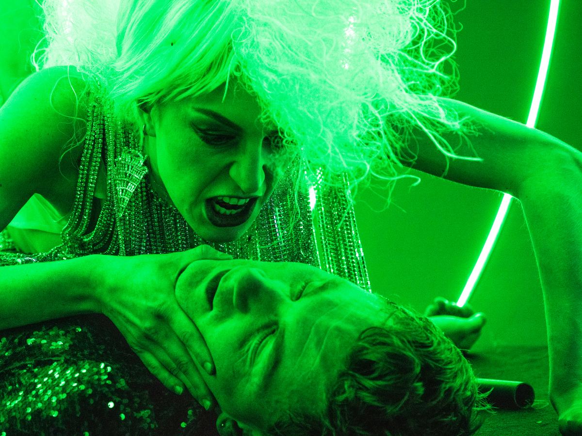 Ein komplett in grünes Licht getauchtes Foto der Schauspielerin Alberta von Poelnitz, wie sie sich über den am Boden liegenden Schauspieler Paul Behren beugt und ihn am Kinn packt / fotografiert von Just Loomis