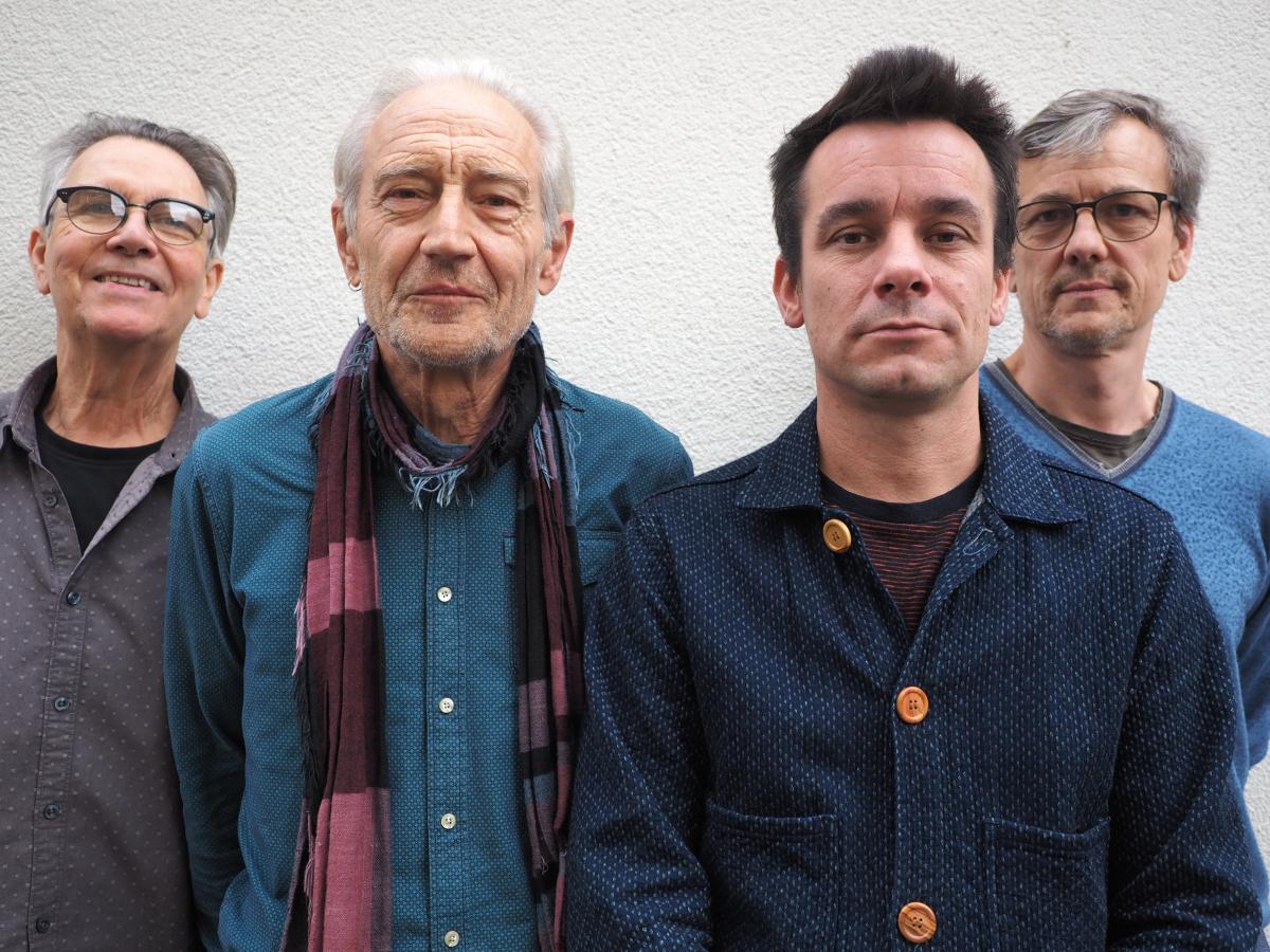 Ruedi Häusermann, Marco Käppeli, Claude Meier, Herwig Ursin stehen eng nebeneinander vor einer weißen Wand und schauen in die Kamera.