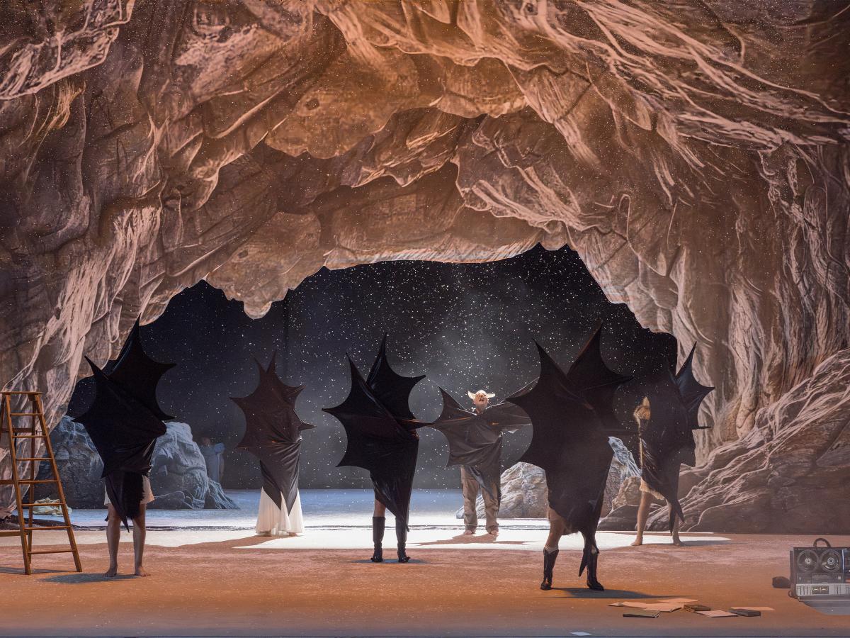 Das Ensemble steht verteilt auf der Bühne in einer Höhle. Alle umarmen sich selbst mit großen schwarzen Fledermausflügeln. Weiße Schnipsel fallen von der Decke.