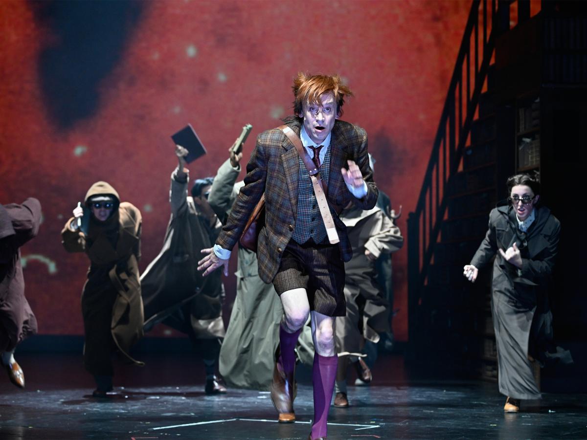 Jan-Peter Kampwirth ist im Vordergrund, hinter ihm mehrere Personen. Alle rennen in Richtung des Publikums und haben die Münder dabei geöffnet. 