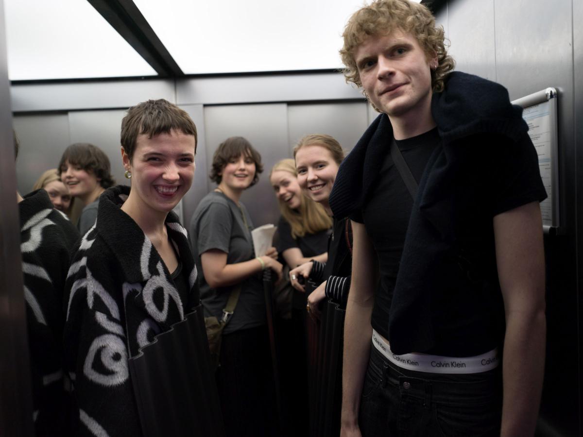 Fünf Jugendliche stehen in einem Aufzug und lächeln und lachen in die Kamera.