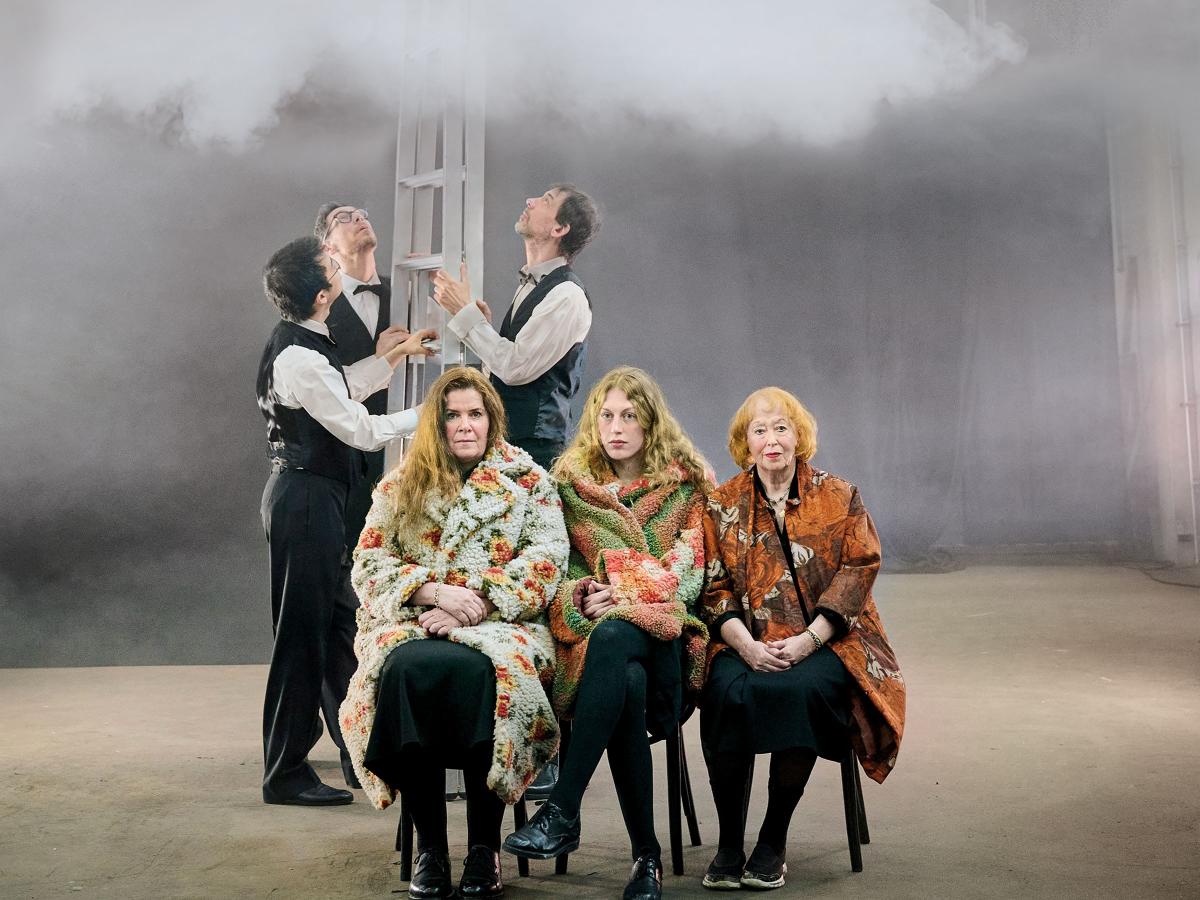 Ankündigungsfoto: Julia Wieninger, Alberta von Poelnitz und Ilse Ritter sitzen in farbig geblümten Mänteln nebeneinander und blicken in die Kamera. Hinter Ihnen stehen Ling Zhang, Stephan Krause und Peter Conradin Zumthor. Sie halten eine Leiter und blicken nach oben. Die Leiter ragt in eine Wolke am oberen Bildrand hinein.