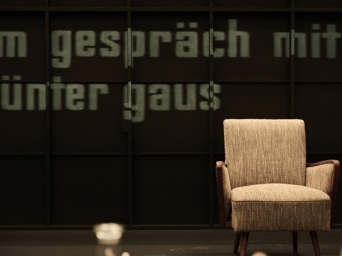 Ein beiger Sessel steht vor einem schwarzen Hintergrund. An der hinteren Wand stehen die Worte "im Gespräch mit Günter Gaus".